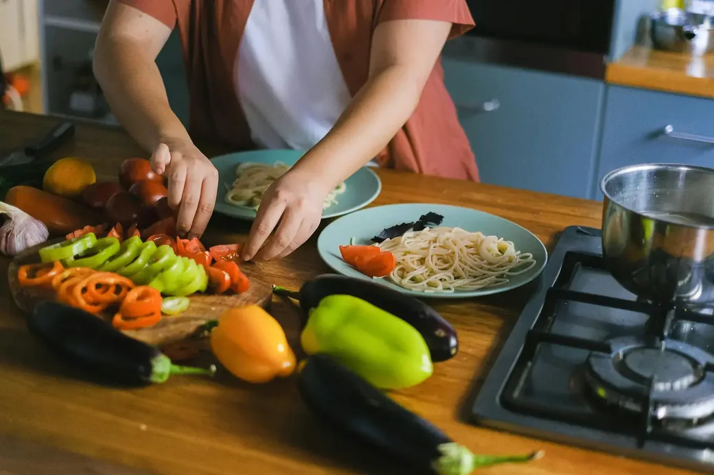 Someone preparing vegetables and pasta at a kitchen counter